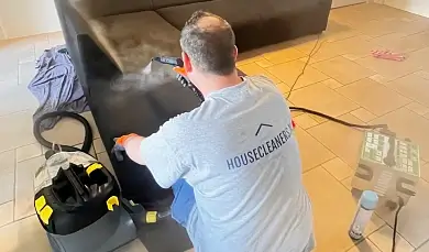 Professional cleaner from Housecleaners.nl steam cleaning the upholstery of a black sofa.